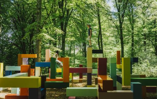 Kinder spielen auf einem mit abstrakten Formen gestalteten Spielplatz in Wanås, umgeben von hohen Bäumen.