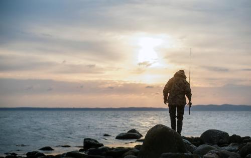 Ein Mann geht bei Sonnenaufgang auf Klippen am Meer angeln