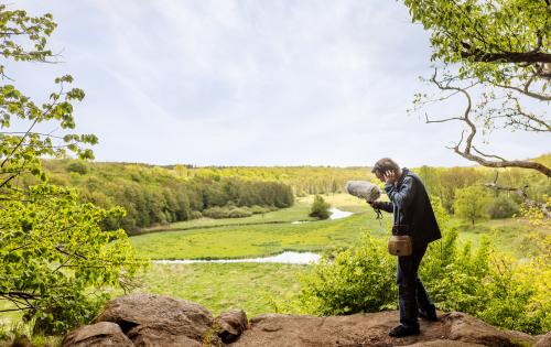 A man standing on top of a rock next to a lush green field and river.