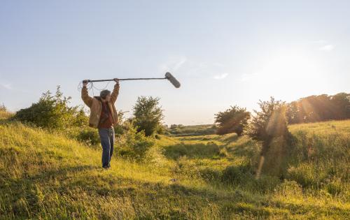 A man holding a microphone on top of a lush green field.
