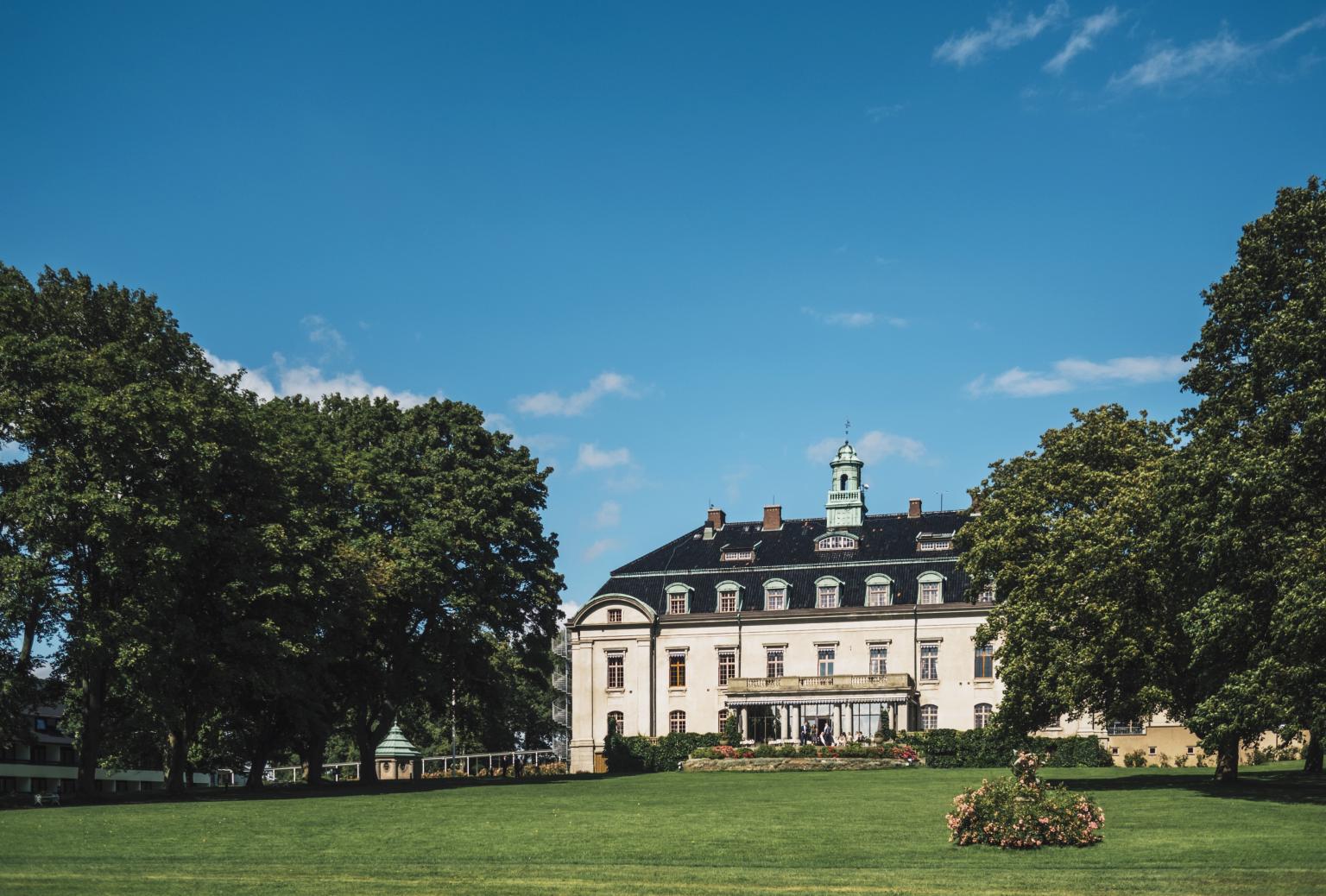 Vitt slott med stor gräsmatta framför och stora träd på sidorna
