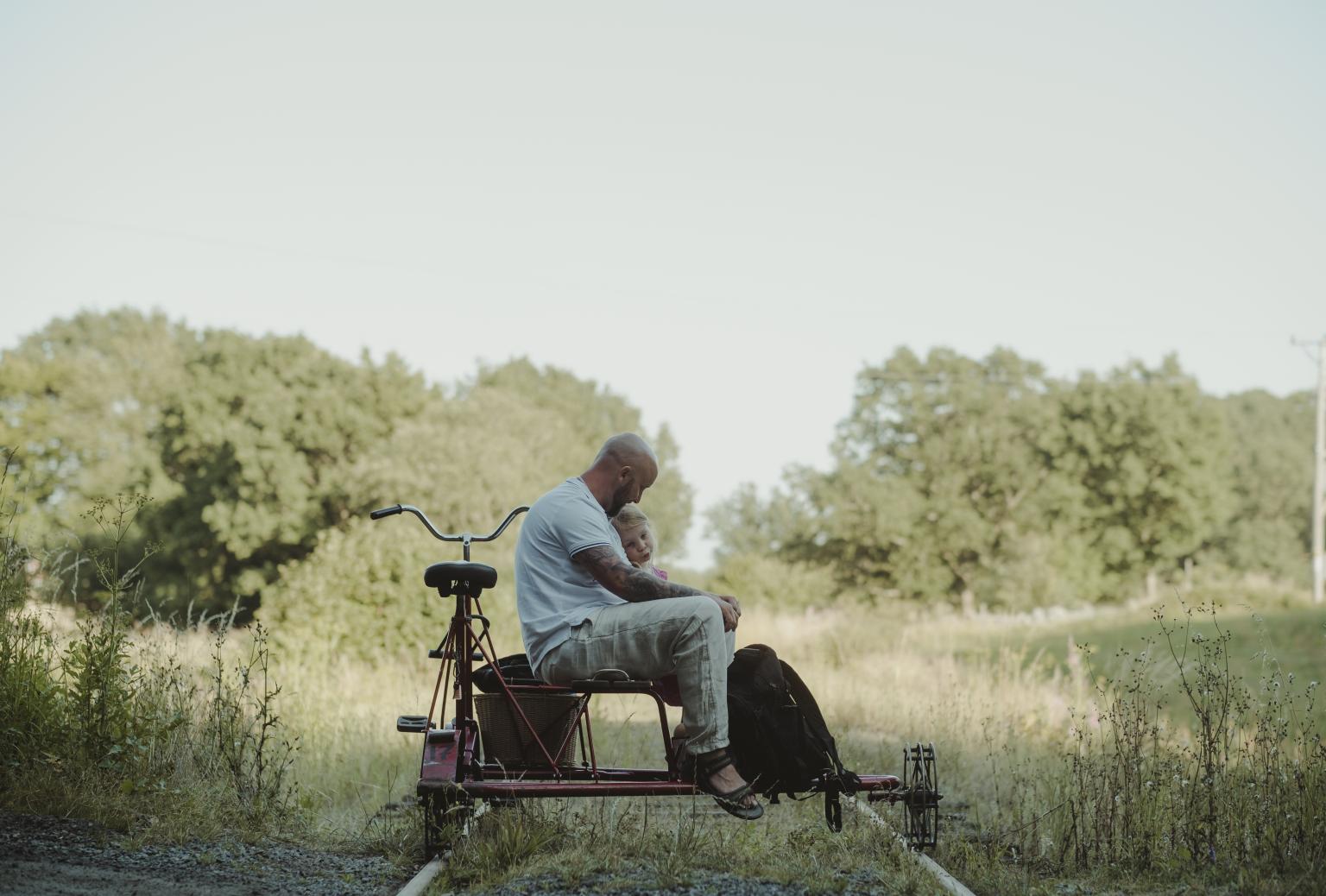 En far sitter tillsammans med sin dotter på en dressin cykel omgiven av naturen