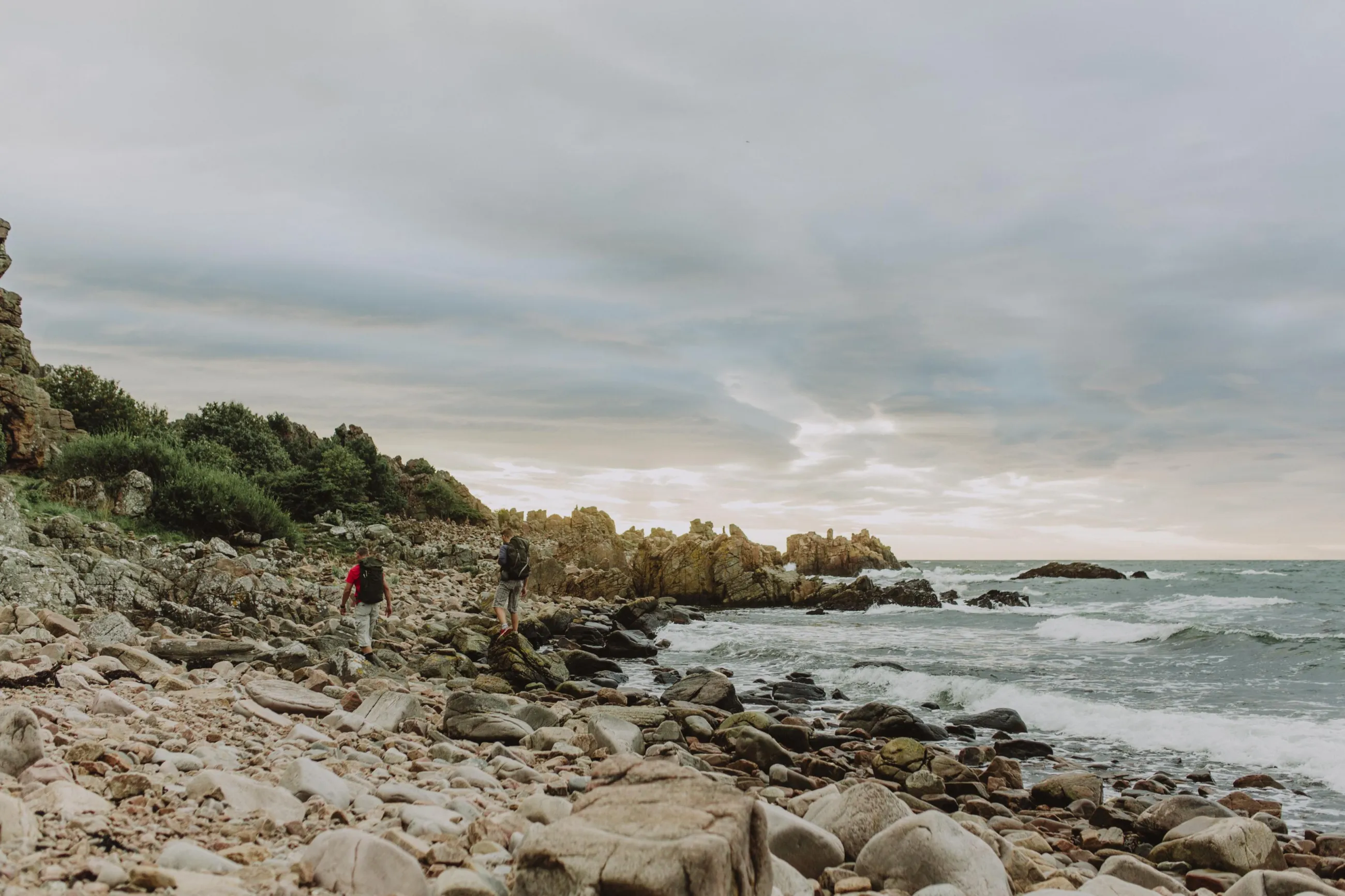 Zwei Männer wandern bei Hovs Hallar an einem Steinstrand mit Felsblöcken entlang.