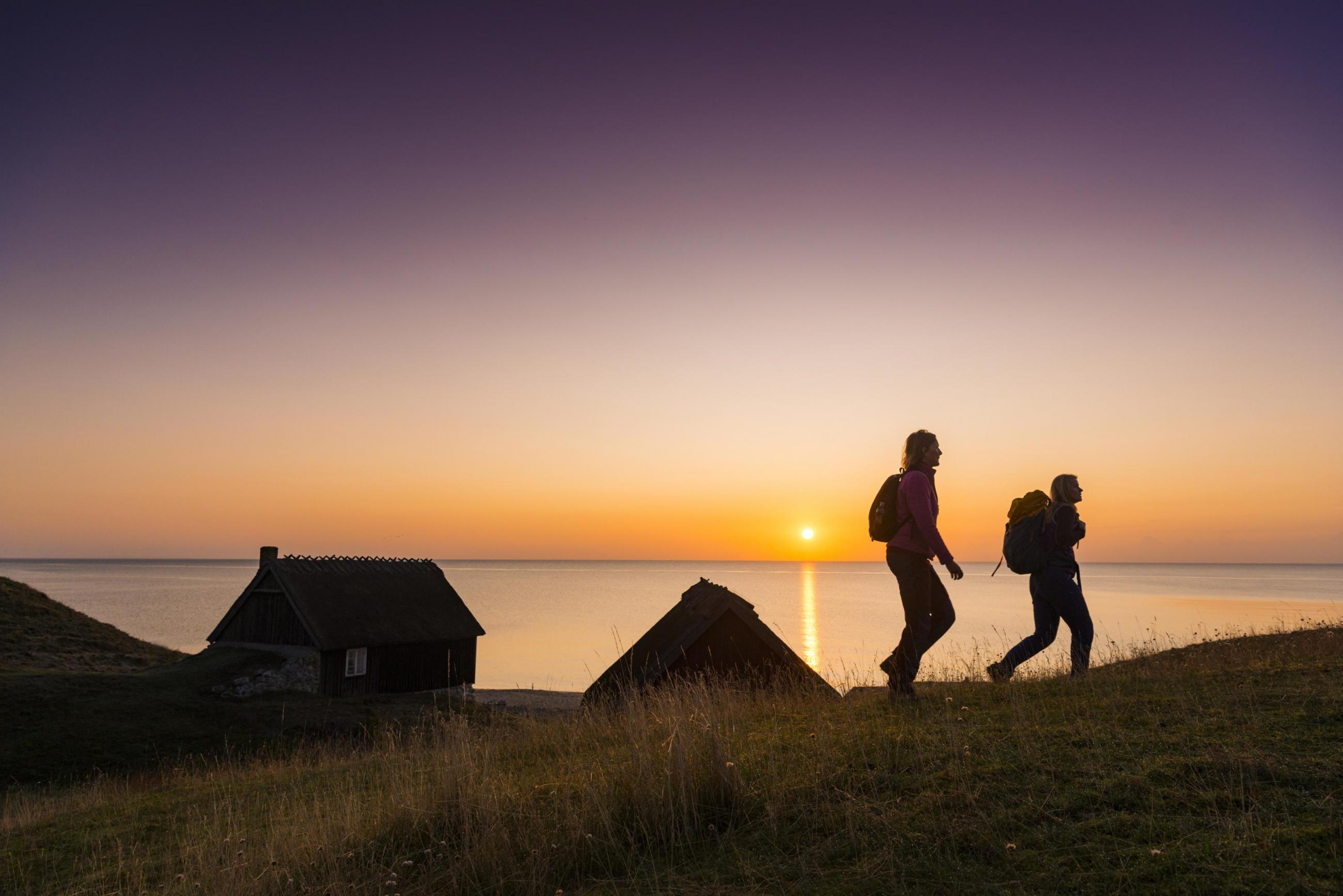 Zwei Frauen spazieren bei Häväng in den Sonnenuntergang und haben das Meer im Hintergrund.