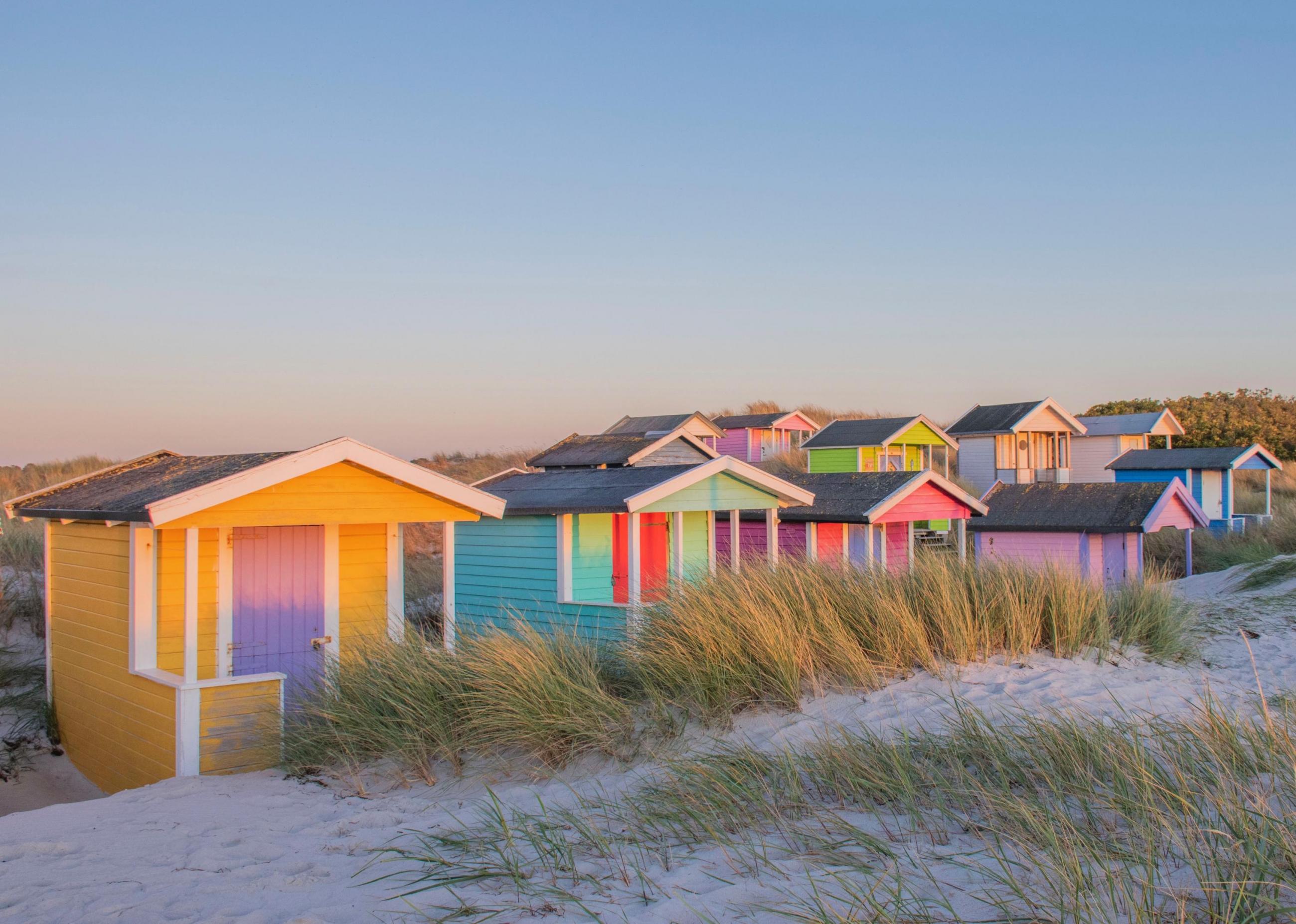 Farbenfrohe Badehütten am weißen Strand von Skanör unter strahlend blauem Himmel