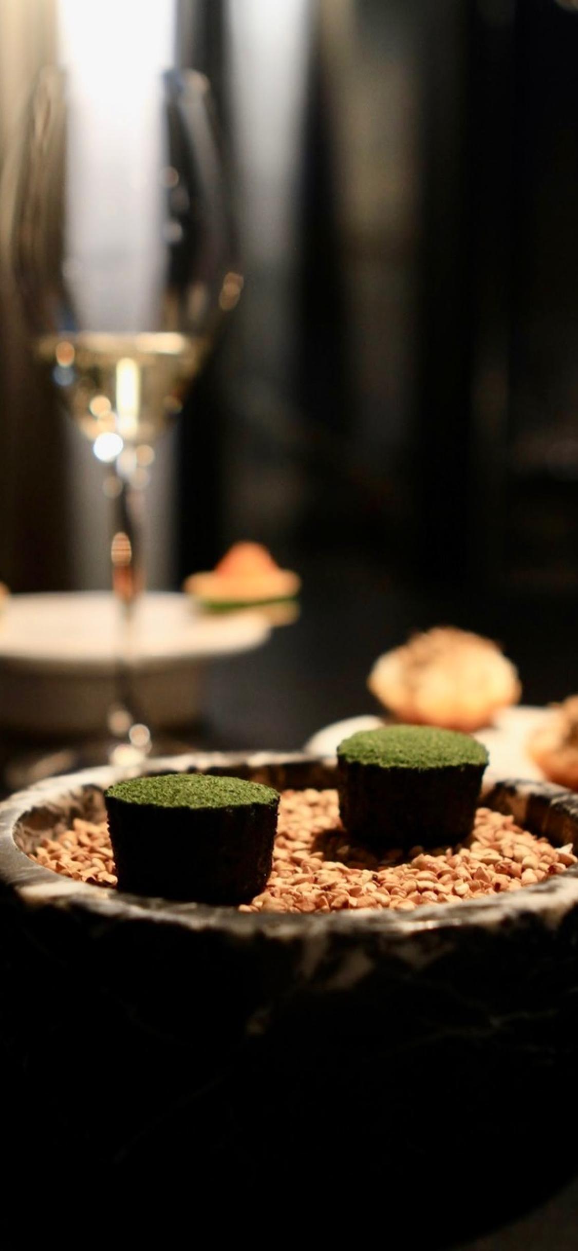 Small appetizers on a dark plate with a glass of wine in the distance