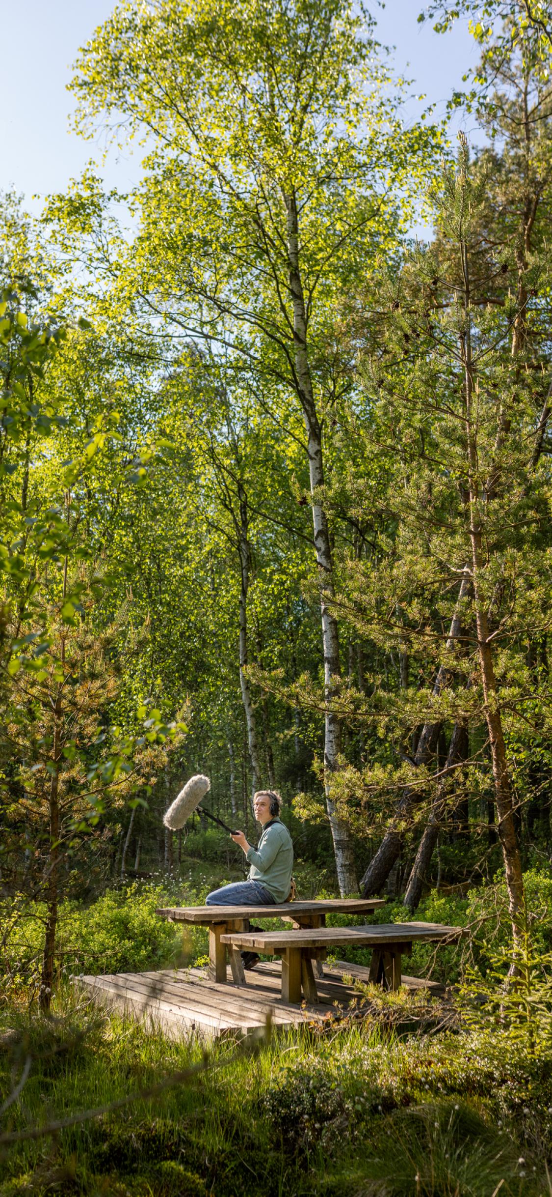 A man sitting on a picnic table in the woods.