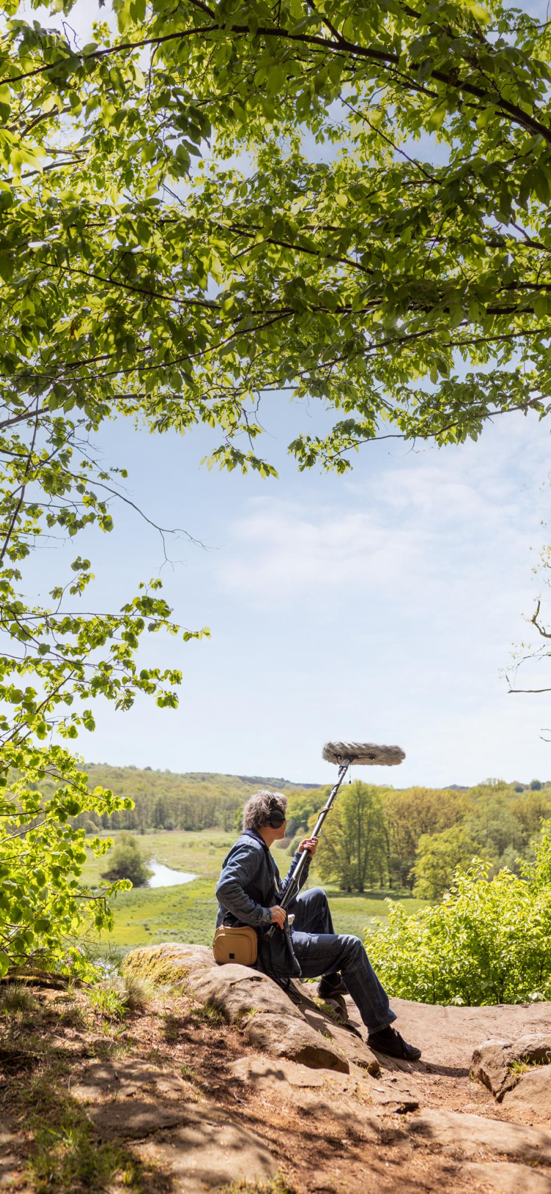 A man sitting on top of a rock next to a forest with view over river.