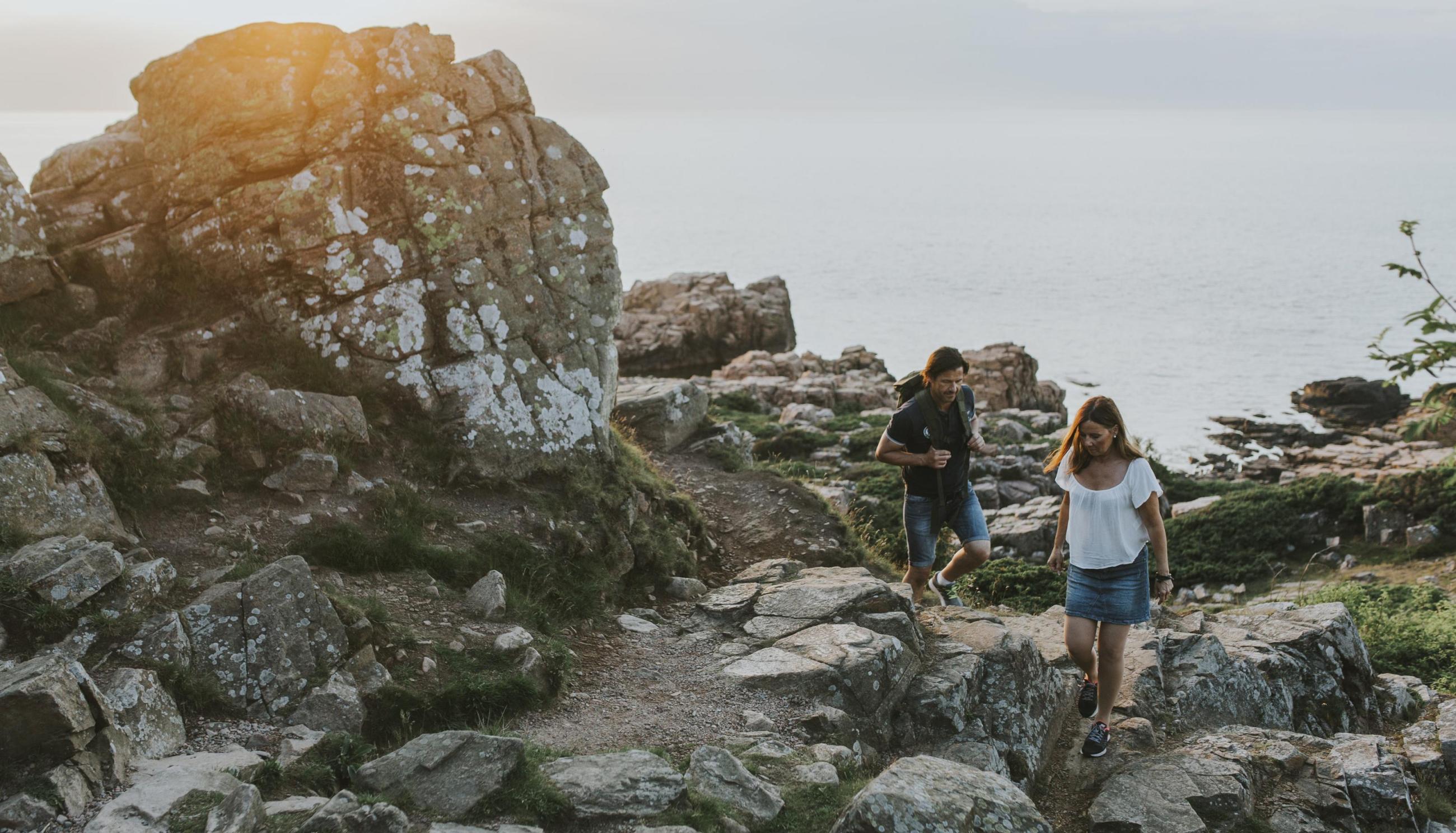 Ein Paar wandert im Naturschutzgebiet Hovs Hallar zwischen Felsen am Meer entlang.