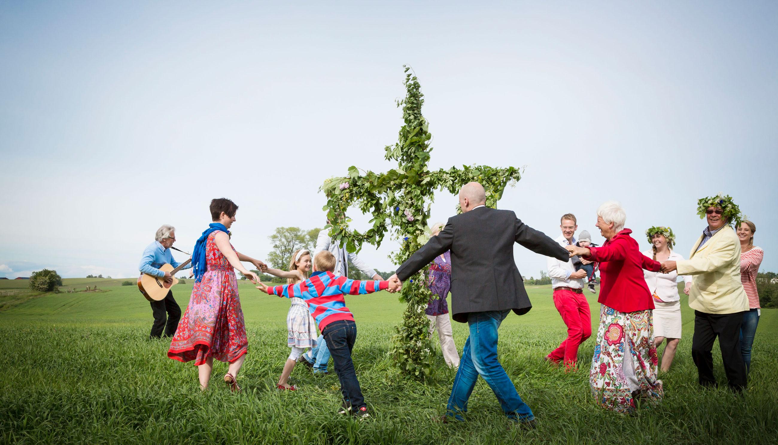 Drei Generationen tanzen um die Mittsommerstange zu den Liedern eines Musikers mit Gitarre.