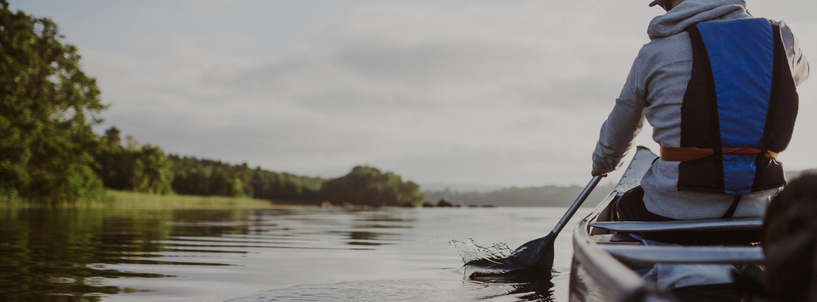 Ein See in Skåne aus der Perspektive des hinteren Paddlers im Zweierkanu.