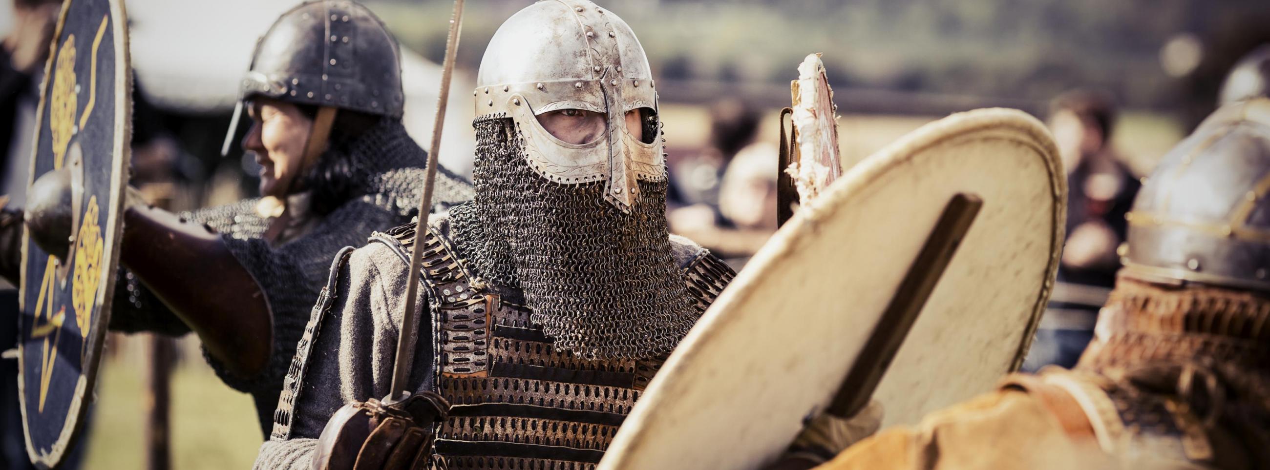 Verkleidete Wikingersoldaten mit Schwertern und Schilden in einem Wikingerdorf.