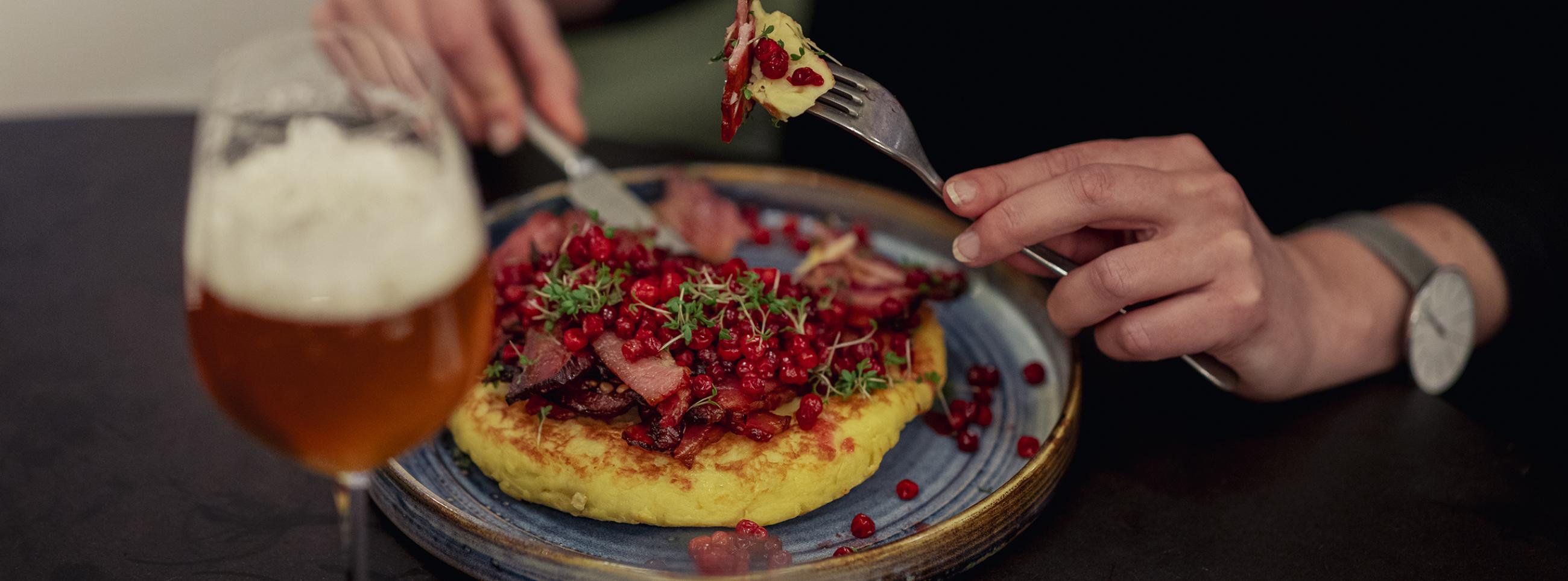 Thick pancake with bacon and lingonberries on top with glass of beer on the side