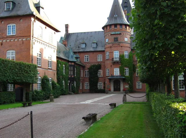 Brick castle with its yard in front and well-kept trees and hedges on the sides