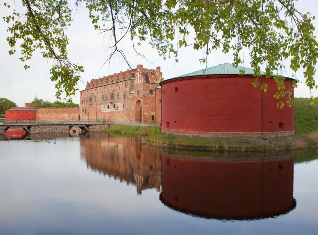Brick castle with red round side building mirroring in the surrounding water