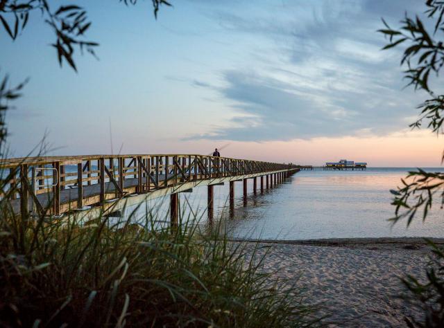 Eine Person geht über den langen Steg zum Freibad und Restaurant in Bjärred.