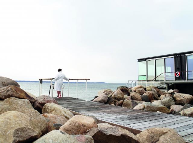 Open-air baths with woman in bathroab walking on pier to swim in the sea