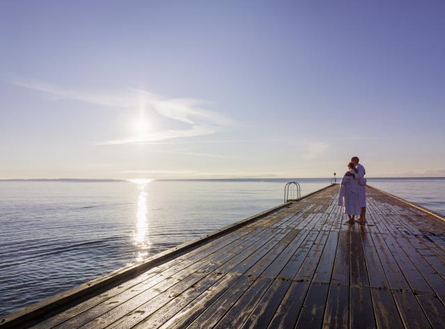 Couple in bathrobes standing on a wooden jetty watching the sunset