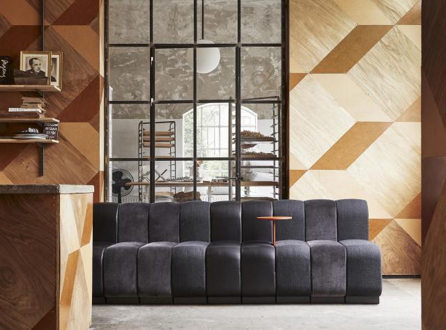 Grey sofa in middle of a wood panneled room with a floor window behind it