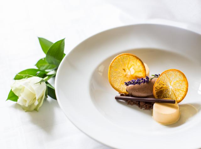 Ein fein angerichtetes Gourmet-Dessert mit Schokomousse und Orangenscheiben, daneben eine weiße Rose, im Schloss Bjärsjölagård.