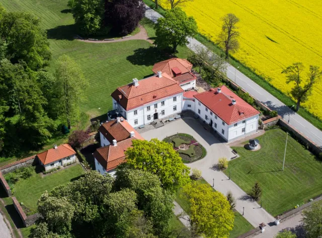 Blick von oben auf das Schloss Bjärsjölagård umgeben von Rapsfeldern, Bäumen und Rasen.