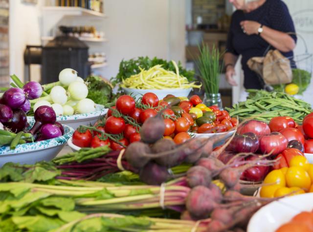 En blandning av grönsaker på ett bord och en kvinna som handlar i bakgrunden