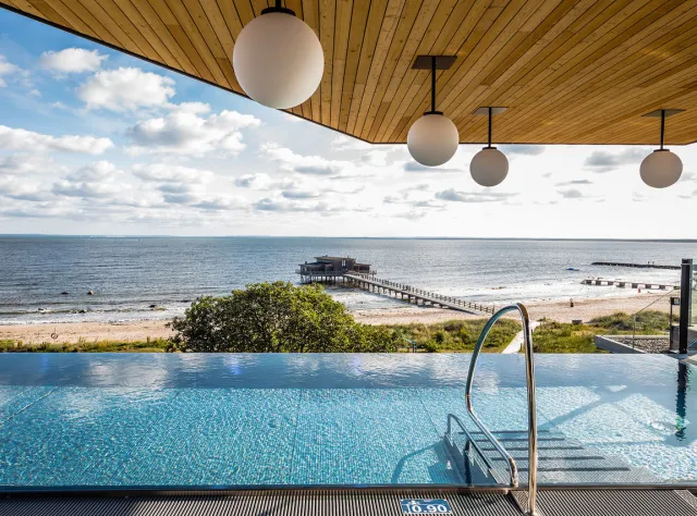 Der Blick von einem Pool auf dem Dach mit dem Strand und einem langen Steg im Hintergrund.