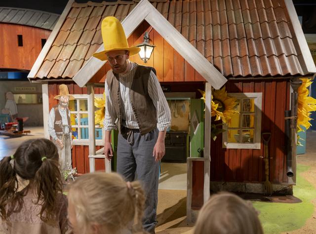 Barn tittar på en man utklädd till Pettson som står framför litet sagohus