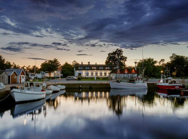 Calm harbor at dusk with mirror-smooth water and a white hotel building in the distance