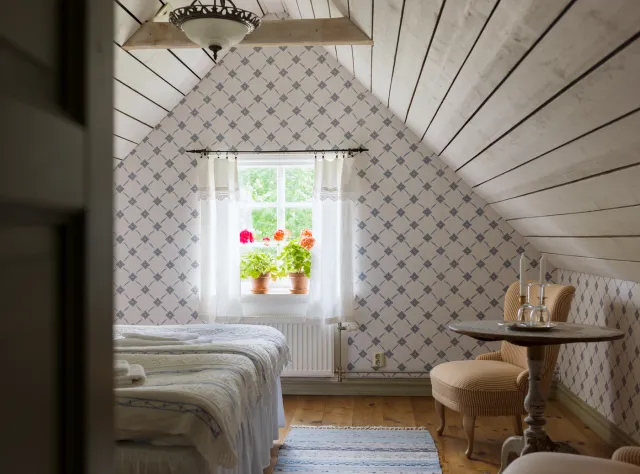 Hotel room with sloped attic ceiling and intricately patterned wallpaper creating a vintage charm