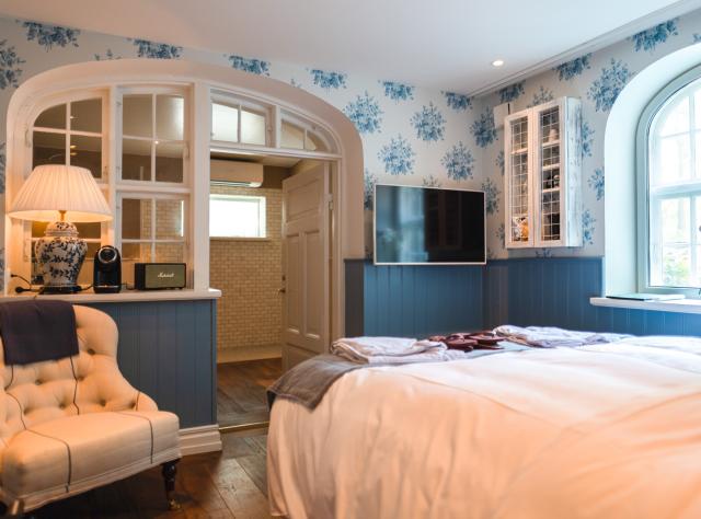 Hotel room featuring arched windows, blue patterned wallpaper, and an inviting bed with plush bedding