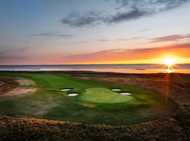 Golfgrün mit Sandbunkern mit Blick aufs Wasser bei Sonnenuntergang, Sonne erzeugt dramatische Strahlen über Küstenlinkskurs mit natürlichen Roughbereichen