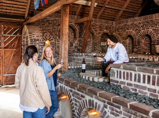 Visitors touring historic brick wine cellar with arched ceiling, examining wine displays while guide explains about wine production in Marani cellar