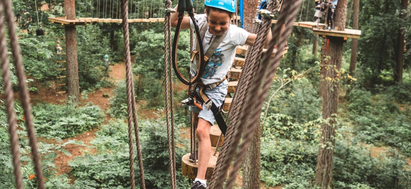 Ein Kind mit Helm klettert im Hochseilgarten Upzone durch die Baumkronen.
