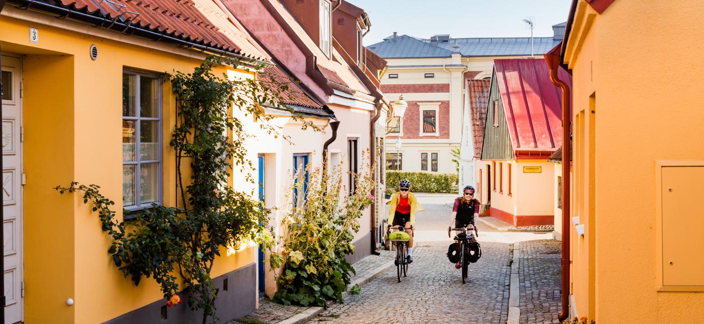  Two cyclists come cycling on a cobbled street among picturesque houses.