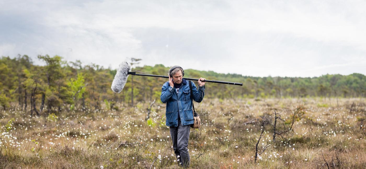 A man in a field holding a microphone.