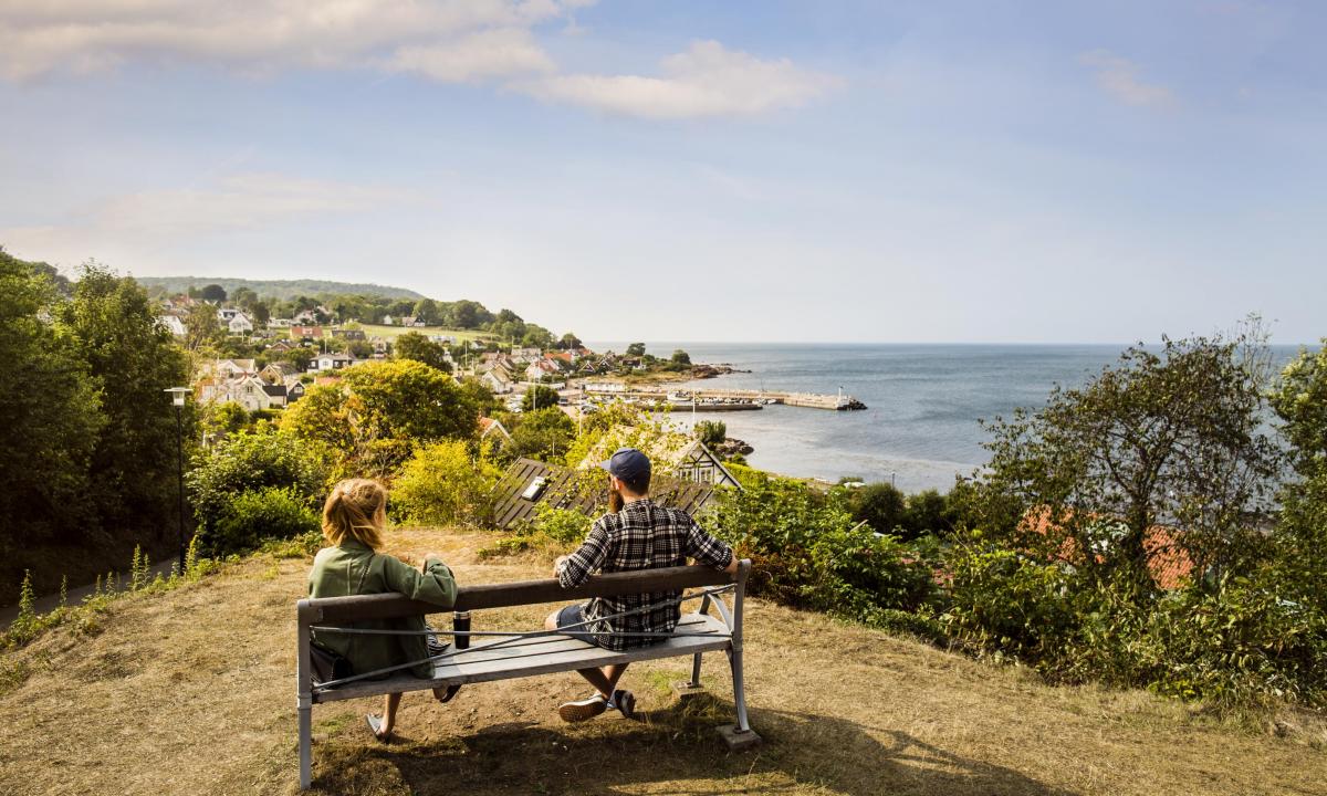 Ein Paar sitzt auf einer Bank mit Blick auf das Küstendorf Mölle.