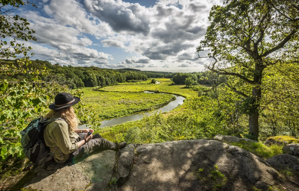 A woman siting on a Cliff overlooking a green valley