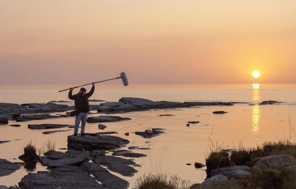 Eine Person steht bei Sonnenaufgang auf Felsen und hält eine Tonangel